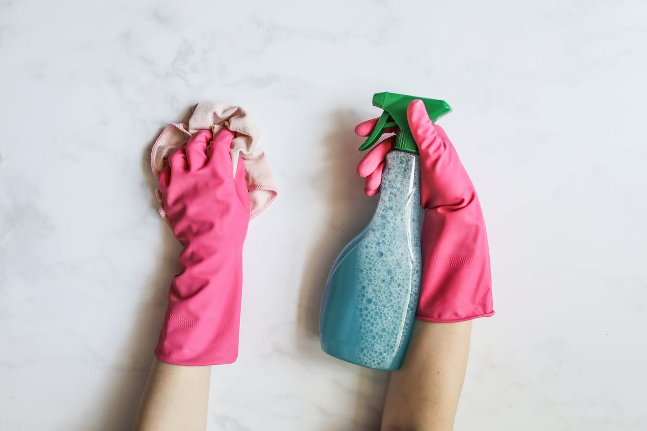 A pair of gloved hands with one holding a cleaning product bottle